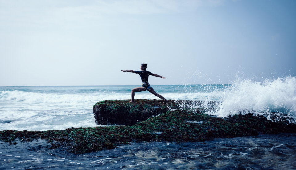 Healthy woman does yoga along a rocky beach