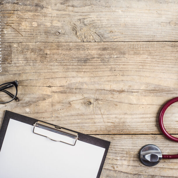 Stethoscope and doctor's clipboard with glasses sitting on a desk.