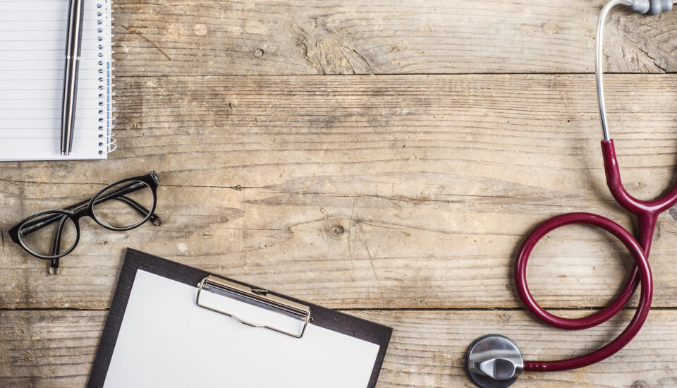 Stethoscope and doctor's clipboard with glasses sitting on a desk.