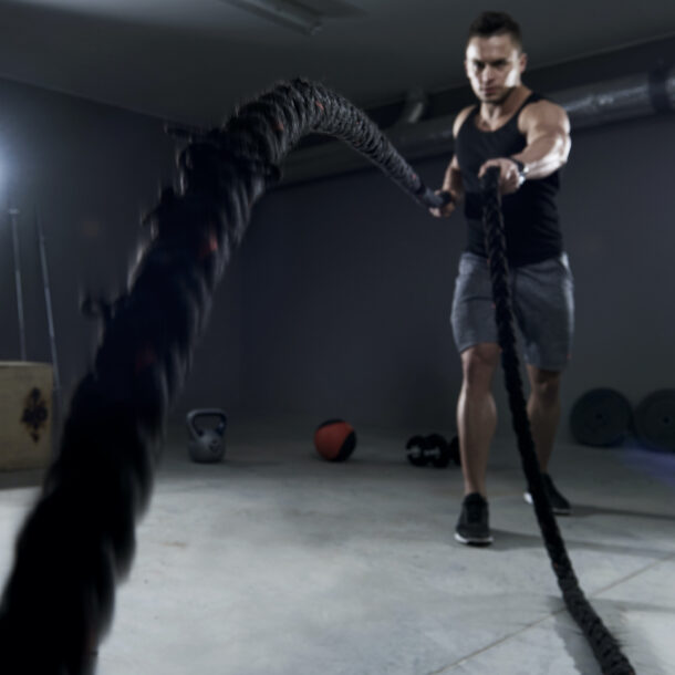 Young man exercising with black battle ropes in a gym setting