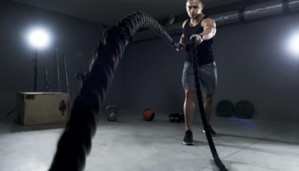 Young man exercising with black battle ropes in a gym setting