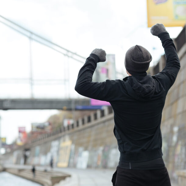 Back view of a man in a hat and gloves standing with raised hands and celebrating success.