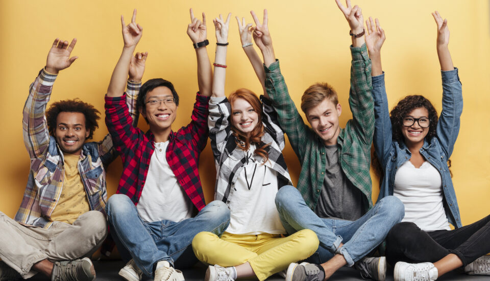 Diverse group of young individuals with their arms in the air celebrating success.