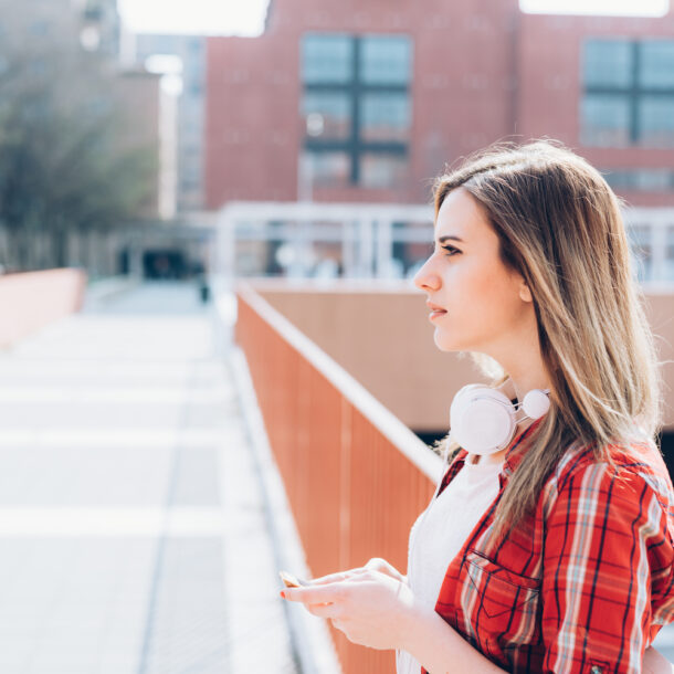 Young woman standing alone in the city contemplating while on her smartphone.