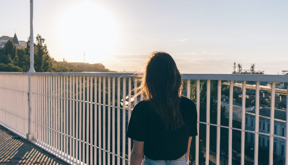 Young woman is walking along the bridge in summer during sunset.