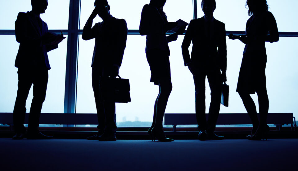 Dark silhouettes of employees standing against a wall of windows.