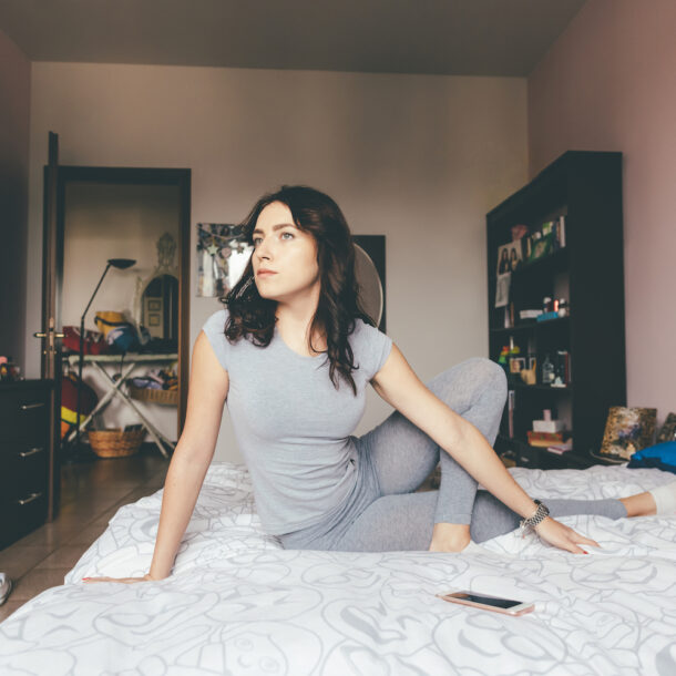 Woman stretching in a meditative pose on her bed.