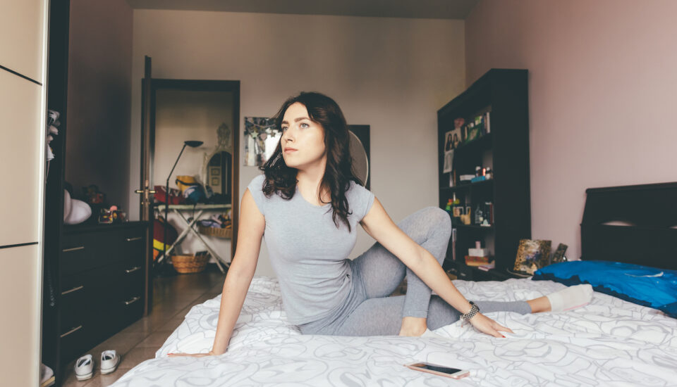 Woman stretching in a meditative pose on her bed.