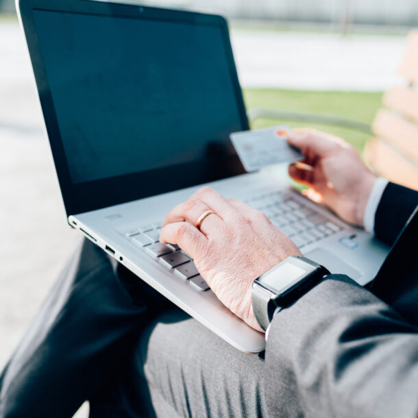 A close-up of a man's hand shopping on a laptop and holding a credit card.