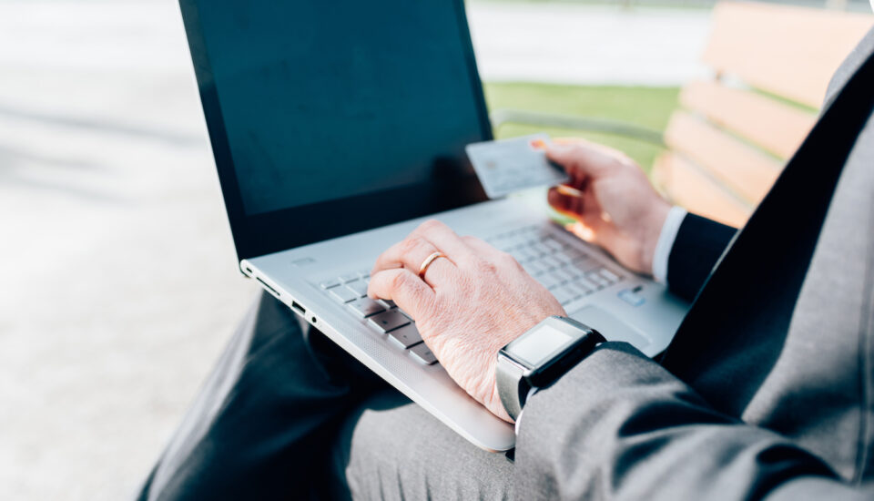 A close-up of a man's hand shopping on a laptop and holding a credit card.