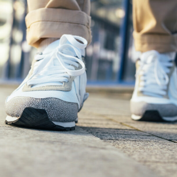 Close up of legs in beige pants and white sneakers walking on the sidewalk.