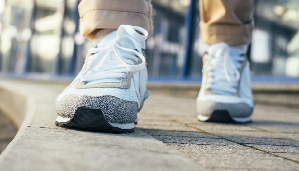 Close up of legs in beige pants and white sneakers walking on the sidewalk.