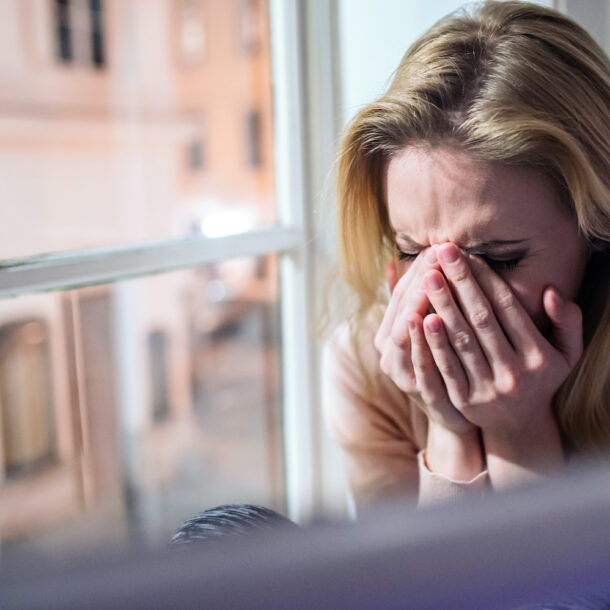 Woman sitting on windowsill, looking out of window, crying.