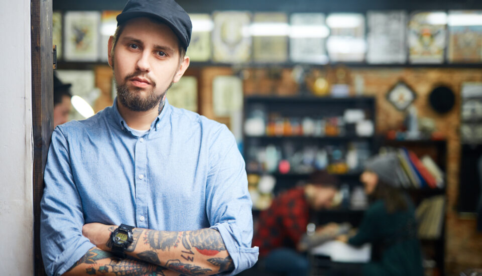 A tattooed man standing alone, contemplating something.