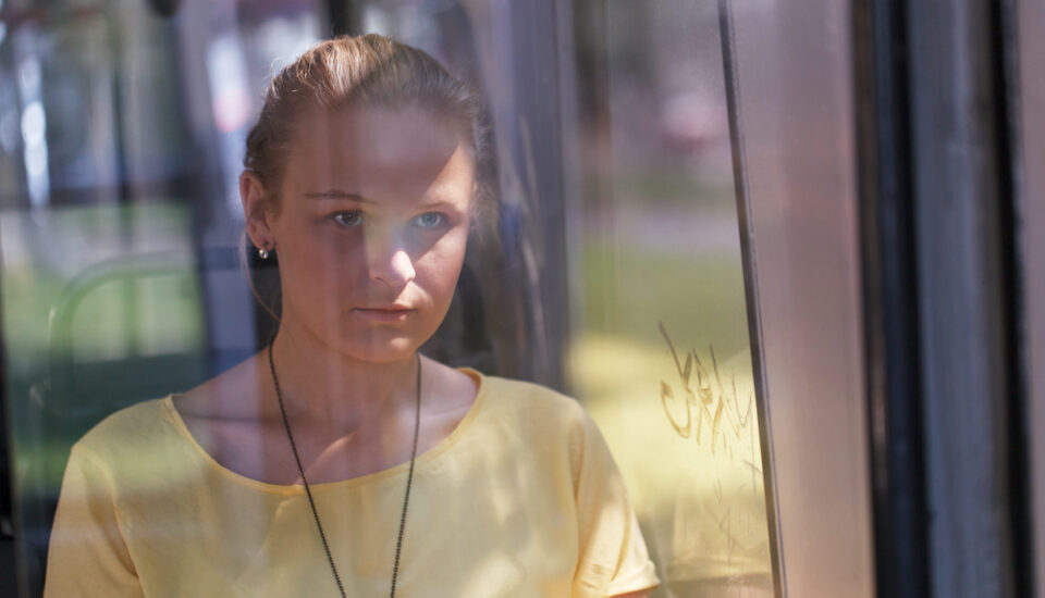 Young woman in yellow rides the bus alone looking out the window.