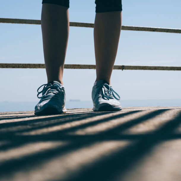 Legs of a young athletic woman in blue sneakers against the railing of a walkway.