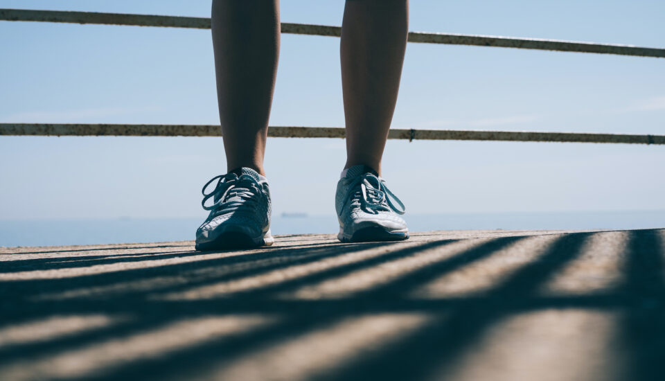 Legs of a young athletic woman in blue sneakers against the railing of a walkway.