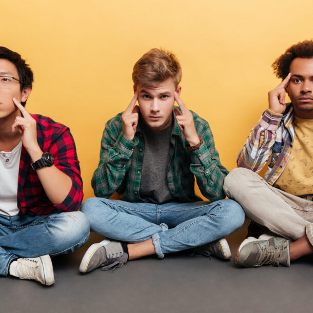 Three tense, stressed young men friends sitting together over yellow background.