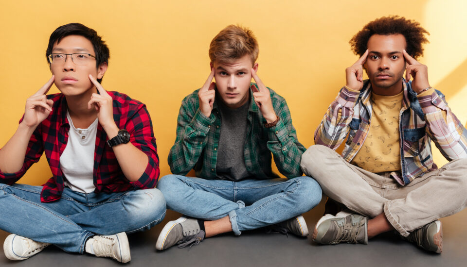 Three tense, stressed young men friends sitting together over yellow background.