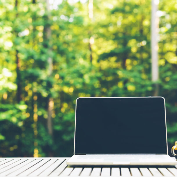 Laptop computer outside with a forest background.