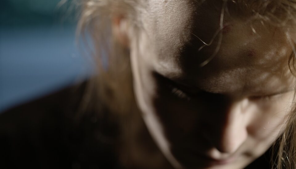 Young person sitting in the dark with a sad look on their face.