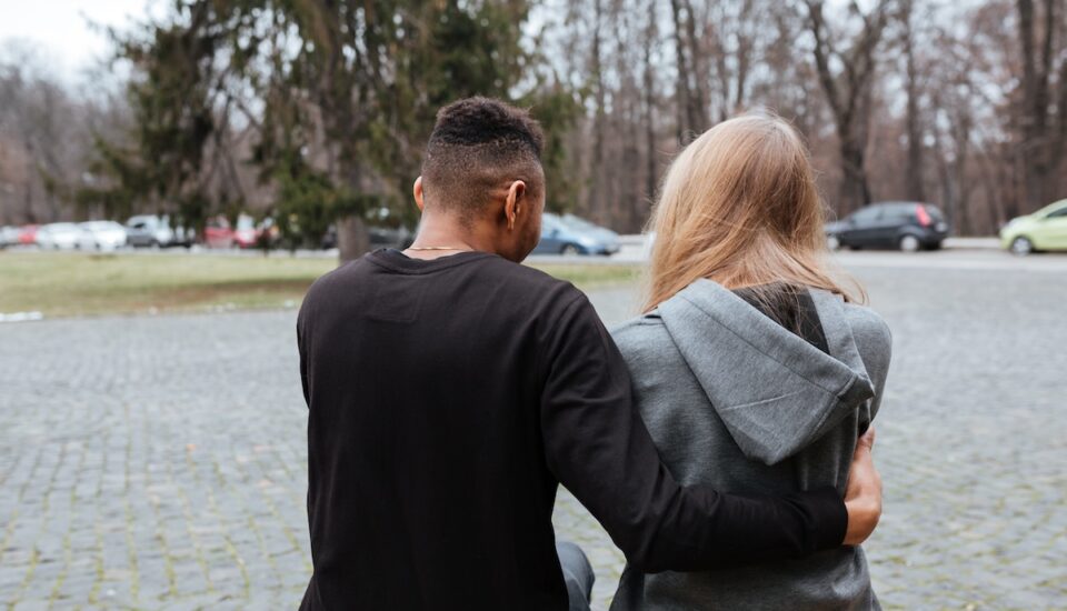 Young multiethnic couple sitting and hugging outside.