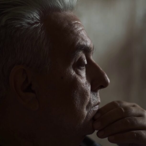 Older man sitting pensively in a dark room.