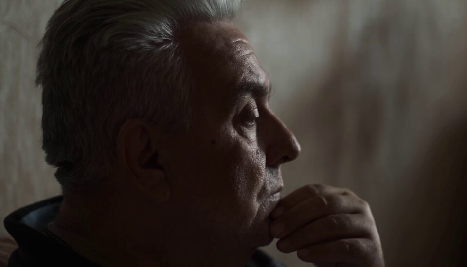 Older man sitting pensively in a dark room.